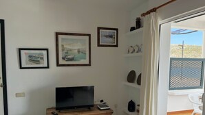 A room with a television on a wooden cabinet, a door leading to an outdoor area, and three framed pictures on the wall.