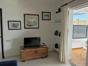 A room with a television on a wooden cabinet, a door leading to an outdoor area, and three framed pictures on the wall. - Apartment in very front line with sea views (Fornells)