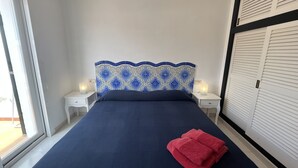 A bedroom with a bed, two bedside tables, a nightstand, a patterned headboard, and a window.