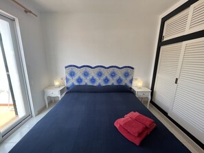 A bedroom with a bed, two bedside tables, a nightstand, a patterned headboard, and a window. - Apartment in very front line with sea views (Fornells)