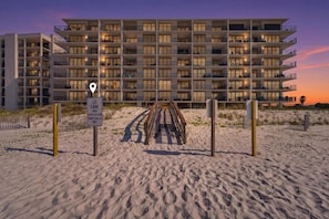 Ein mehrstöckiges Hotel mit Balkonen, Zugang zum Strand und Blick auf den Sonnenuntergang.