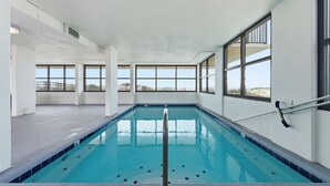 Une piscine intérieure avec de grandes baies vitrées, un sol carrelé et un escalier pour entrer dans l’eau.