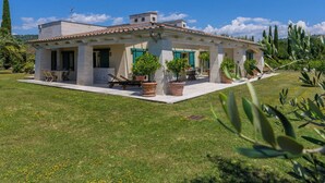 Una casa de dos pisos con un patio, plantas en macetas y un cielo azul despejado.