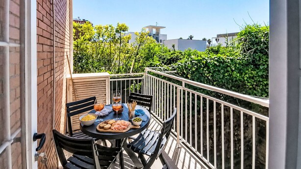 Ein Balkon mit Tisch, Stühlen und Geländer, gedeckt für eine Mahlzeit.