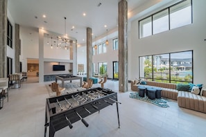 A spacious living area with a foosball table, a sofa set, and a large window offering a view of the outdoors. - Landing | Spectacular 1BD, Yoga Studio, Gym (Pooler)