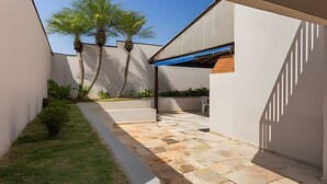 A modern outdoor patio area with a stone floor, a small lawn, and a few trees. - Coberturinha Massa (São Paulo)