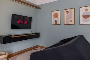 Uma sala de estar com uma TV fixada na parede exibindo 'NETFLIX', um móvel de entretenimento preto e três quadros na parede.