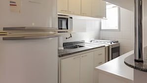 A modern kitchen with white cabinets, a built-in microwave, and a stainless steel refrigerator. - Coberturinha Massa (São Paulo)