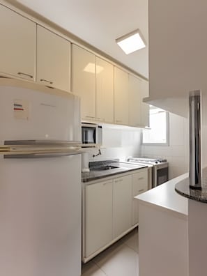 Una cocina moderna con armarios blancos, microondas integrado y refrigerador de acero inoxidable.