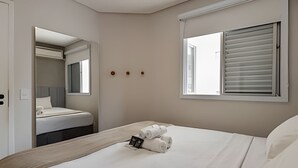 A hotel room with a bed, a window with blinds, a mirror, and a door. - Coberturinha Massa (São Paulo)