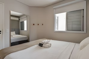 Una habitación de hotel con cama, ventana con persianas, espejo y puerta.