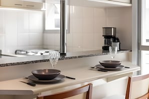 A modern kitchen with a white countertop, two dark bowls, a knife, and a glass.