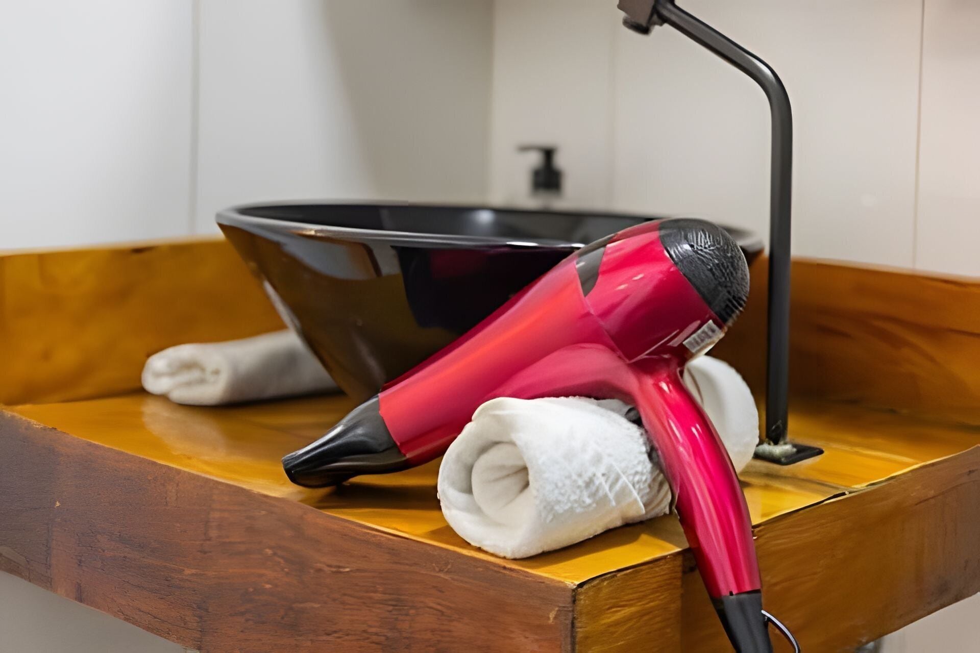 A bathroom with a wooden vanity, a black basin, and a red hairdryer.