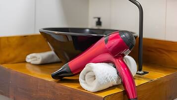 A bathroom with a wooden vanity, a black basin, and a red hairdryer.