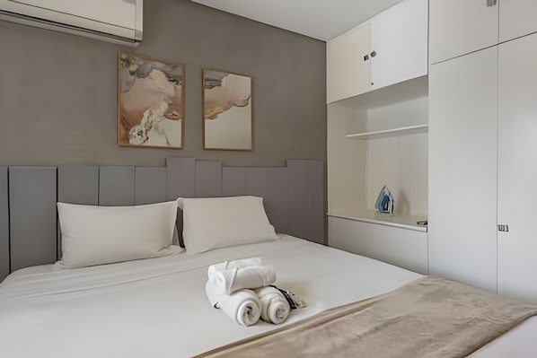 Una cama bien hecha con ropa blanca, un cabecero gris y dos cuadros abstractos en la pared.