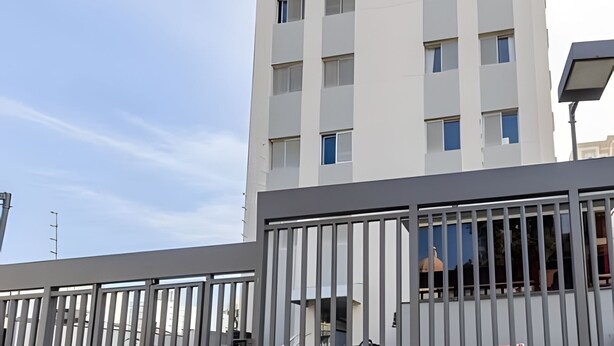 A modern building with a white facade, multiple windows, and a metal fence in the foreground. - Coberturinha Massa (São Paulo)