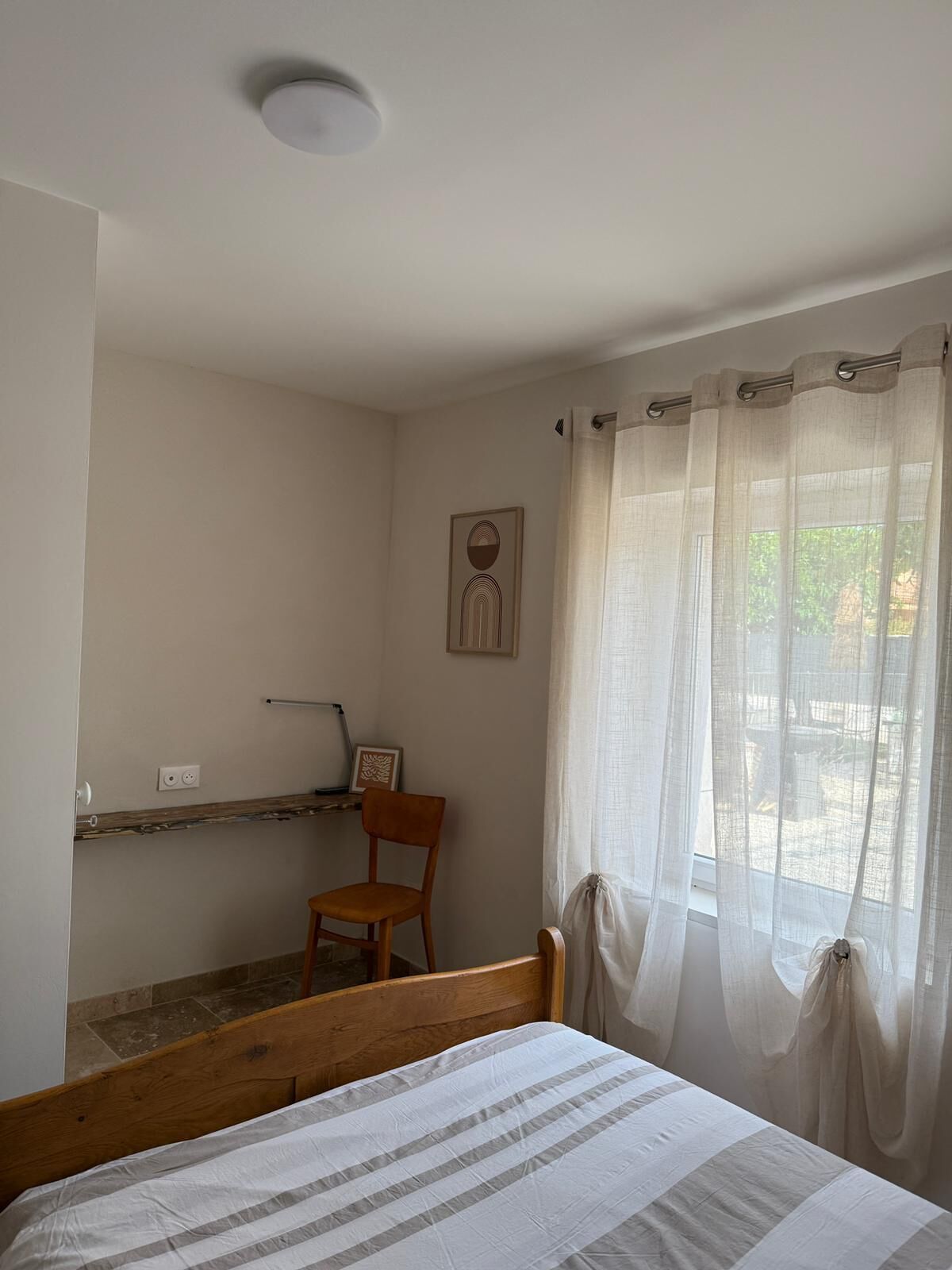 A bedroom with a bed, a chair, a shelf, and a window with curtains.