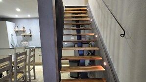 A modern staircase with wooden steps and metal railings, leading to a dining area with wooden chairs and tables. - Peaceful charming house (Lapalud)