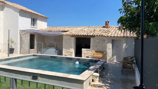 A swimming pool with a tiled deck, a covered patio, and a stone wall. - Peaceful charming house (Lapalud)