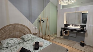 A bedroom with a bed, a bedside table, a hanging light fixture, a mirror, and a bathroom with a sink and mirror. - Peaceful charming house (Lapalud)