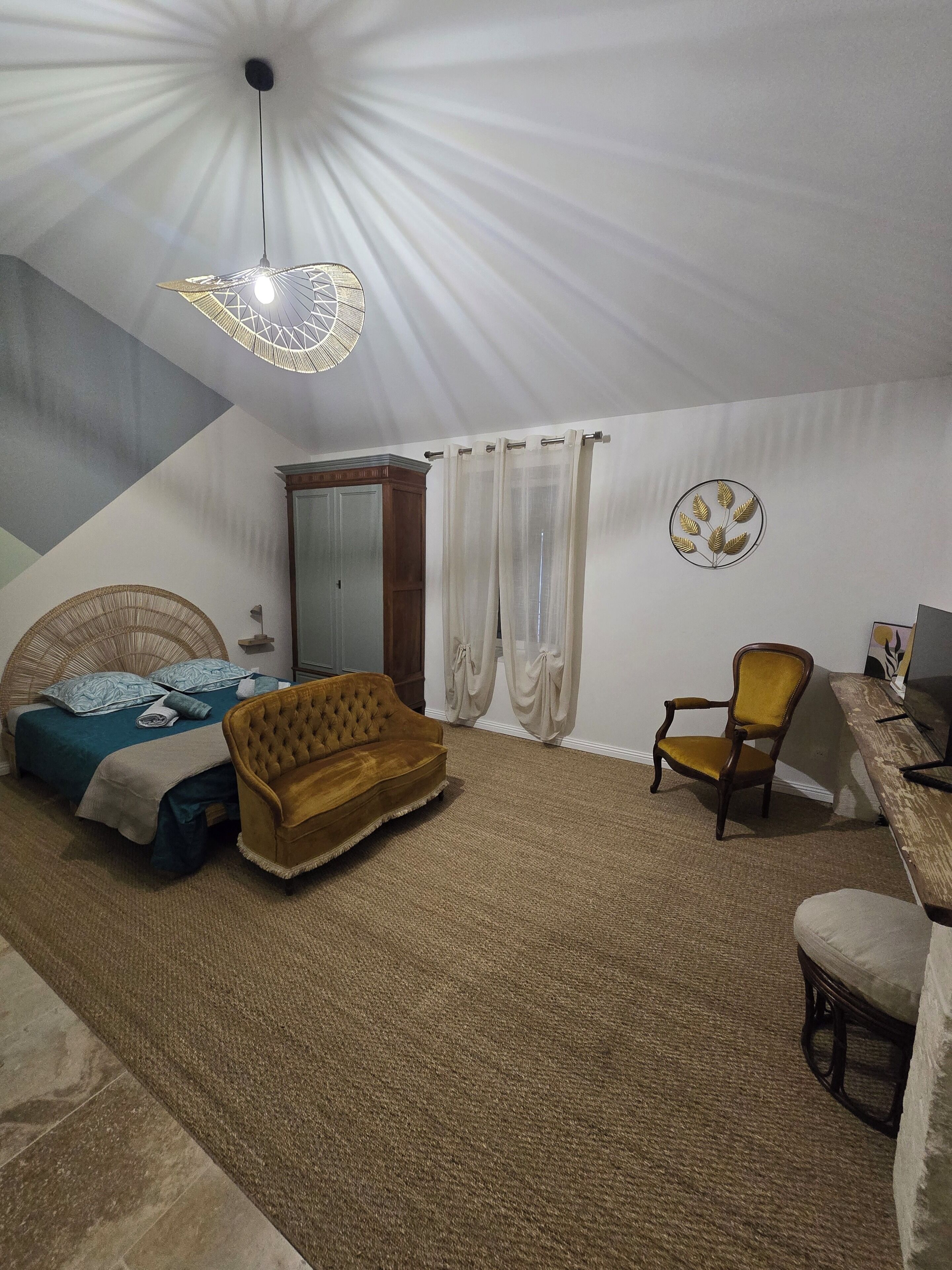 A bedroom with a bed, a sofa, a chair, a desk, a lamp, and a ceiling fan.