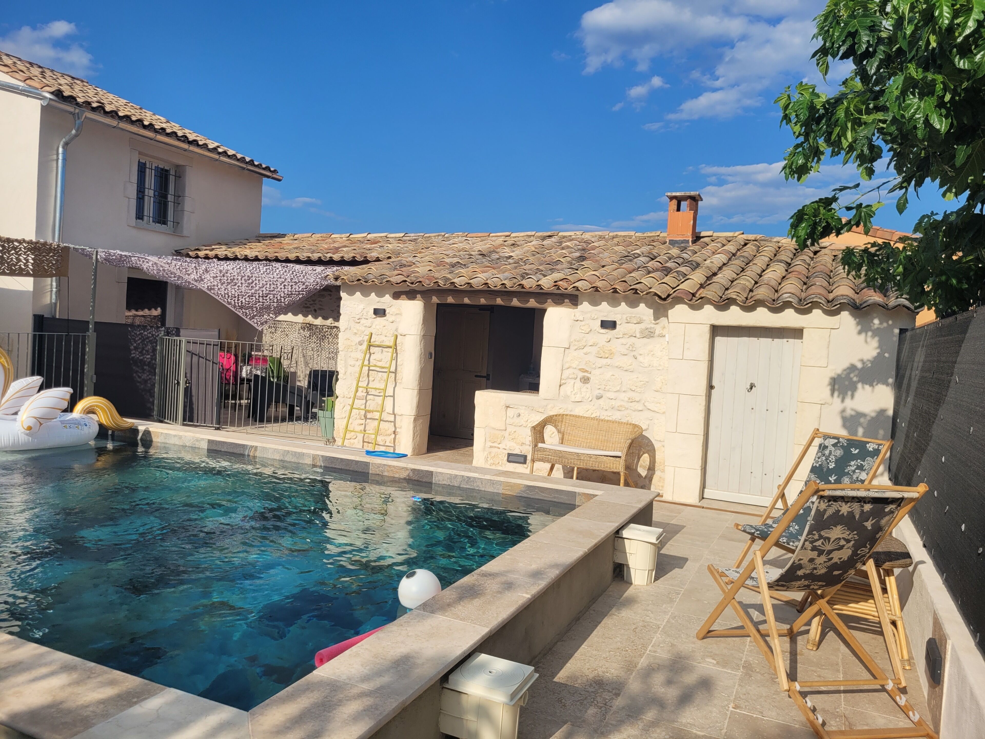 A swimming pool with a stone wall, a ladder, and a chair.
