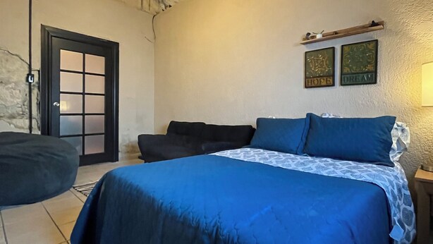 A bedroom with a large bed, a wooden ceiling, a door with frosted glass panels, and two wall-mounted artworks.