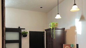 A room with a dark wooden cabinet, a small wooden table with a lamp, two black stools, a patterned rug, and a door with frosted glass panels.