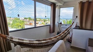 Ein Zimmer mit einer Hängematte, großen Fenstern, Blick auf Gebäude und einem Balkon.