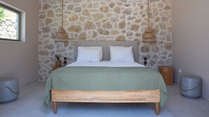 A bedroom with a stone wall, a bed with a green bedspread, two hanging lamps, and a window. - Village Escape House by CorfuEscapes (Corfu)