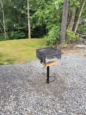En grill på en grusoverflade med græs og træer i baggrunden.
