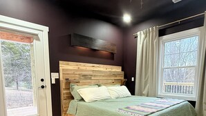 A bedroom with a wooden bed, a bench, a window with curtains, and a door. - 2 King beds! Sleep like royalty in this cozy, intimate, and brand-new house (Scottsville)