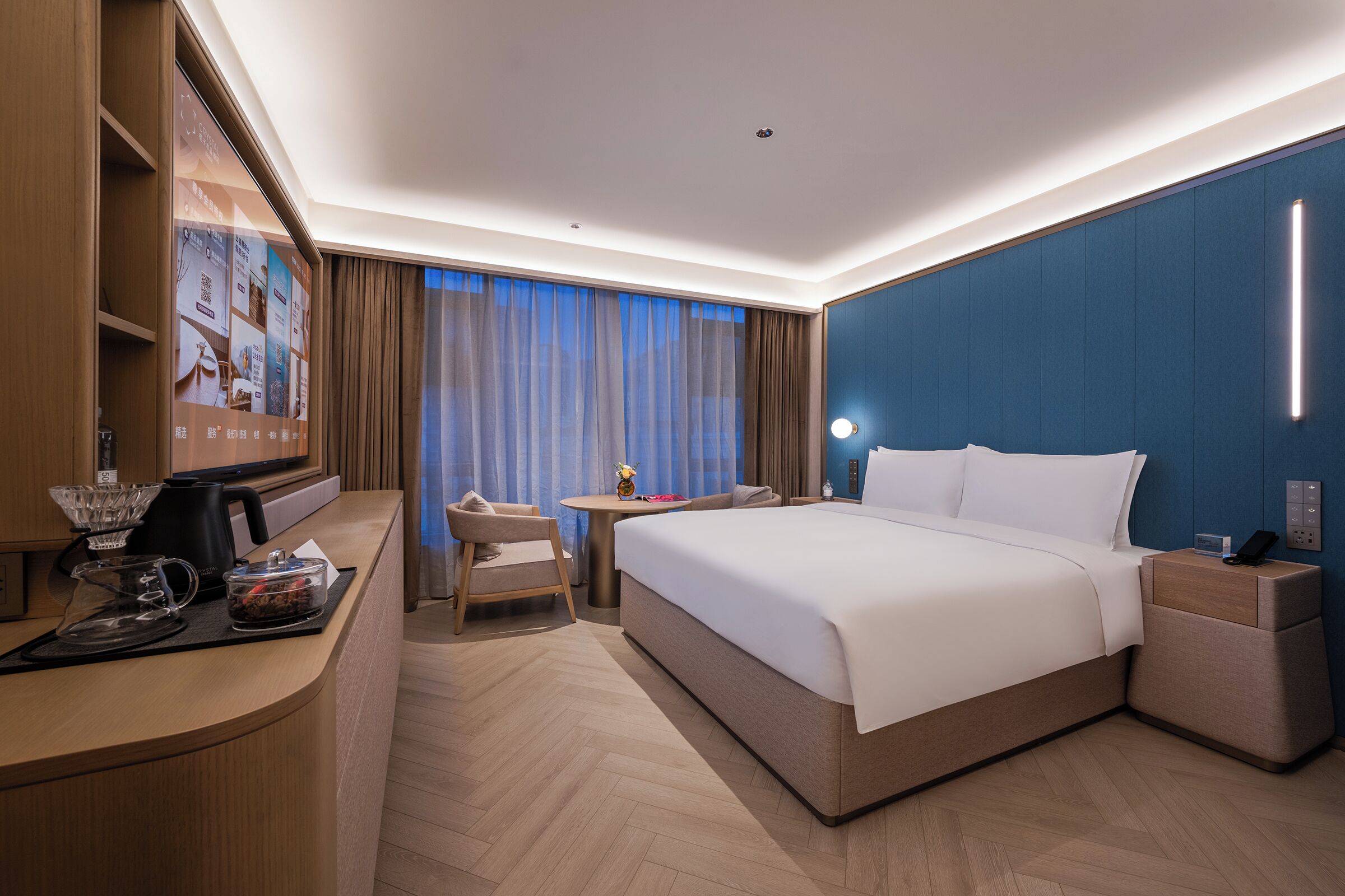 Habitación de hotel con cama, mesita de noche, escritorio, silla y televisor.