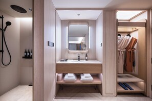 Um banheiro moderno com chuveiro, toucador com espelho e um closet com roupas penduradas.