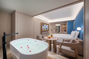 Et moderne hotelværelse med et stort badekar, en seng, et lille bord med frugt og et fjernsyn.