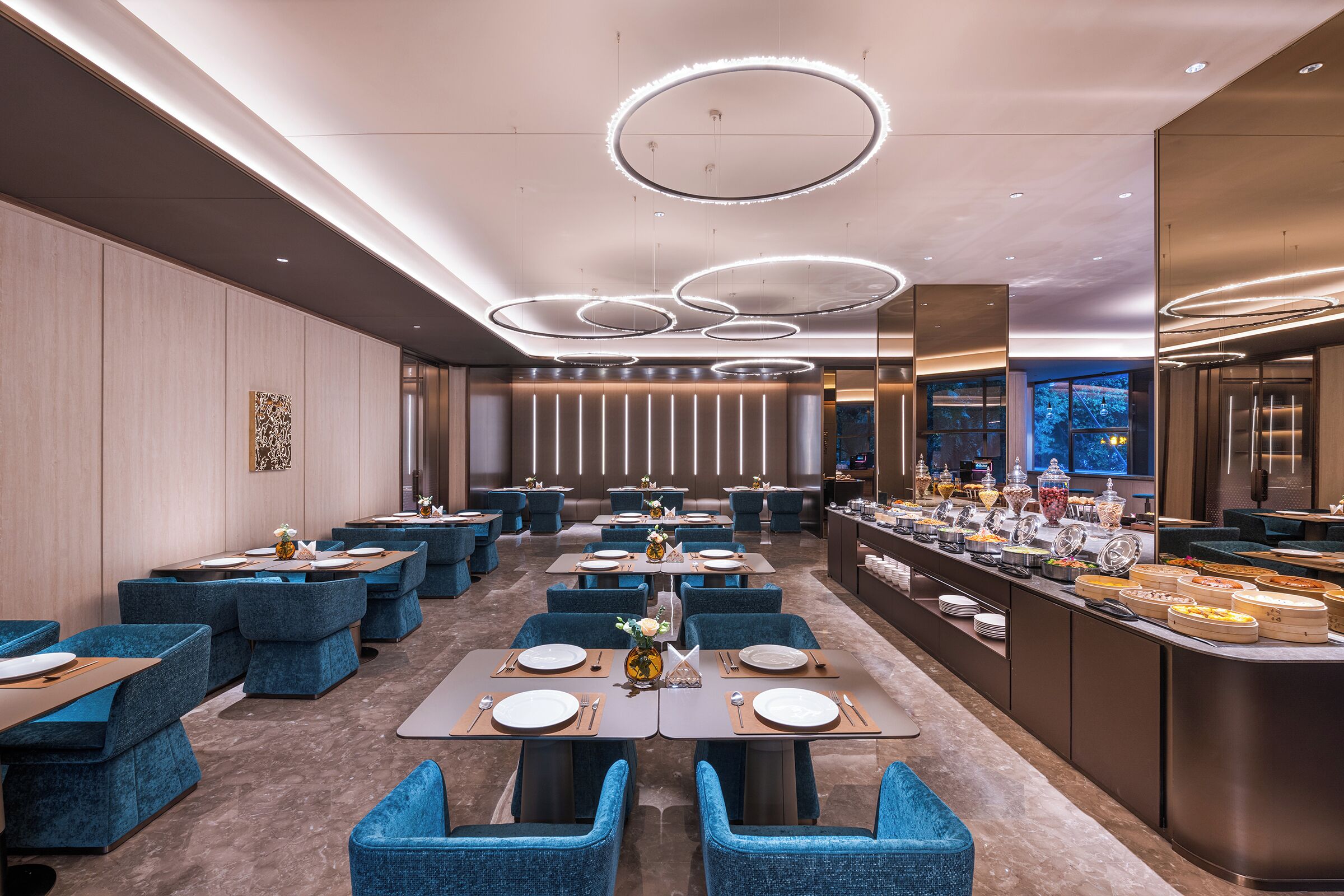 A modern restaurant with blue upholstered chairs, round tables, and a buffet area.