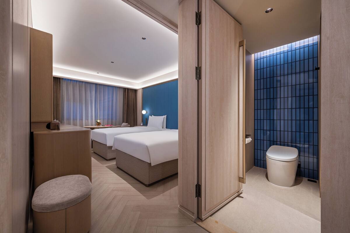A hotel room with a bed, bedside table, and a bathroom with a toilet and shower.