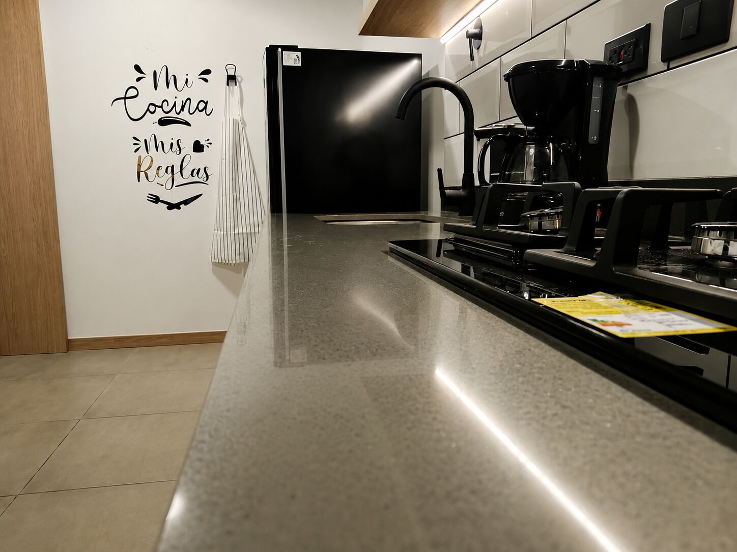 Une cuisine moderne avec un réfrigérateur noir, une machine à café et un porte-serviettes fixé au mur.