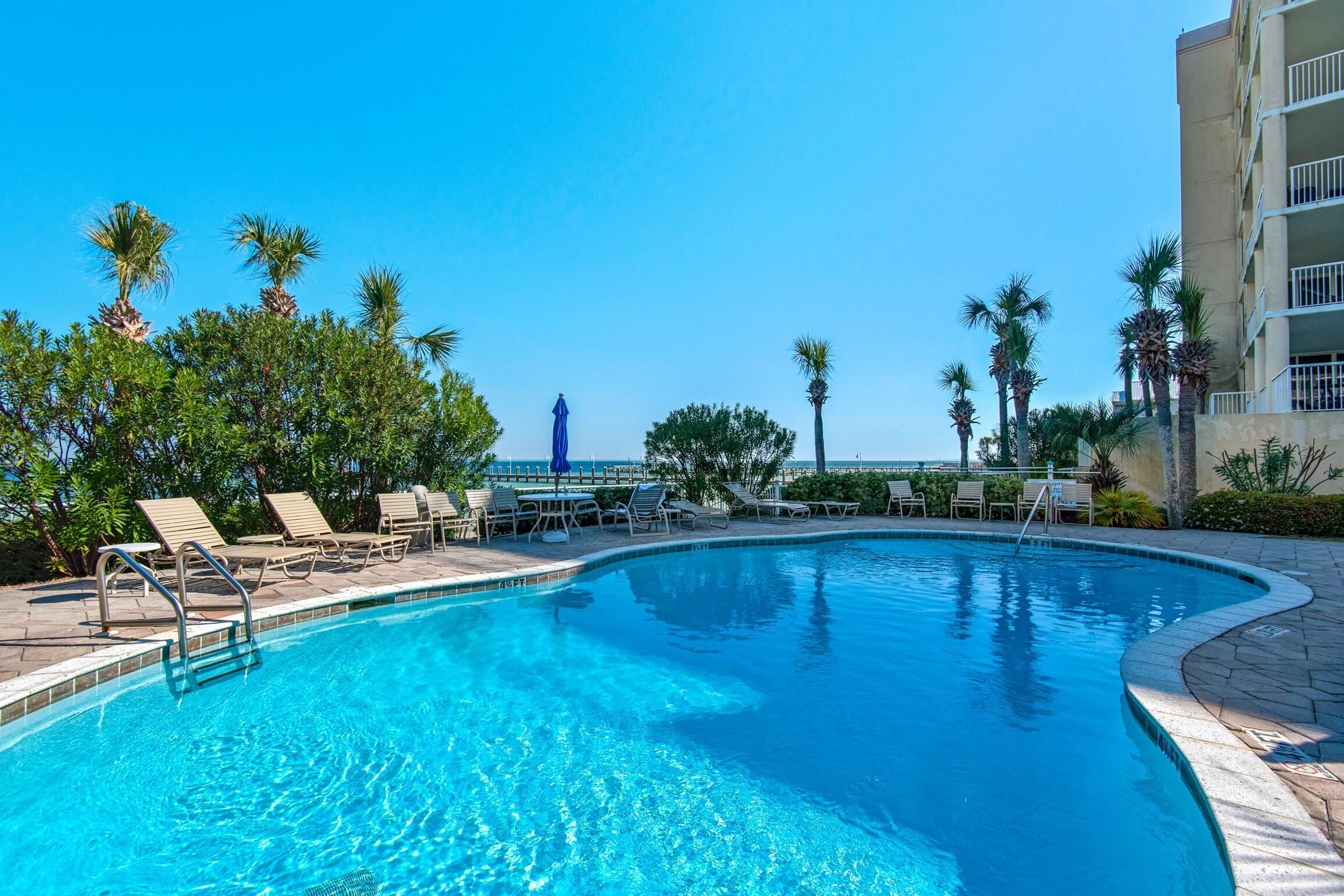 A swimming pool with lounge chairs and palm trees, surrounded by a building with balconies.