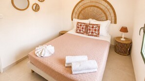 Une chambre à coucher bien aménagée, avec un grand lit, une tête de lit ronde en osier et une petite table de chevet avec une lampe.