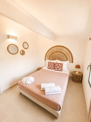A neatly arranged bedroom with a large bed, a round wicker headboard, and a small side table with a lamp. - Résidence ANTONIA - Attic apartment with pool access - Calvi town center (Calvi)