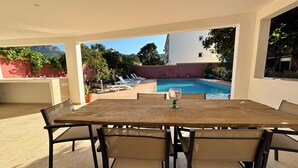 Une terrasse extérieure avec une piscine, des chaises longues et une table avec des chaises.