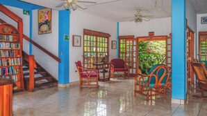 A spacious room with a staircase, a bookshelf, and a dining area with chairs and a table. - Hotel Gracia (San Juan del Sur)