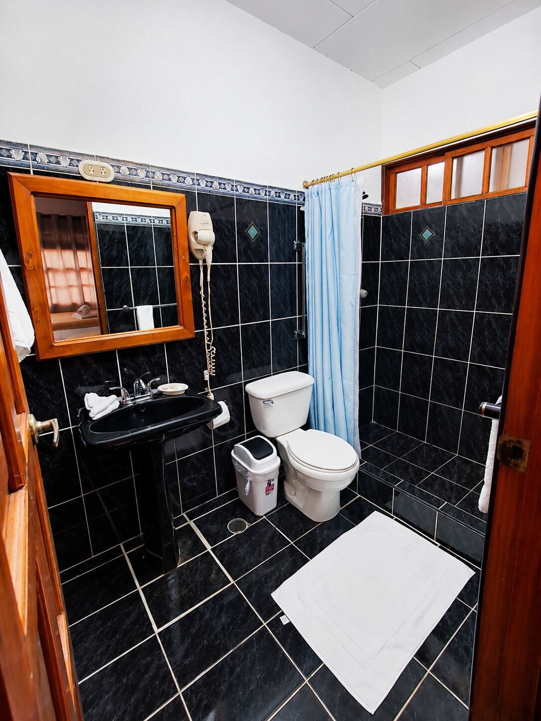 Casa de banho com chão em mosaico preto, lavatório branco, sanita e cortina de chuveiro.