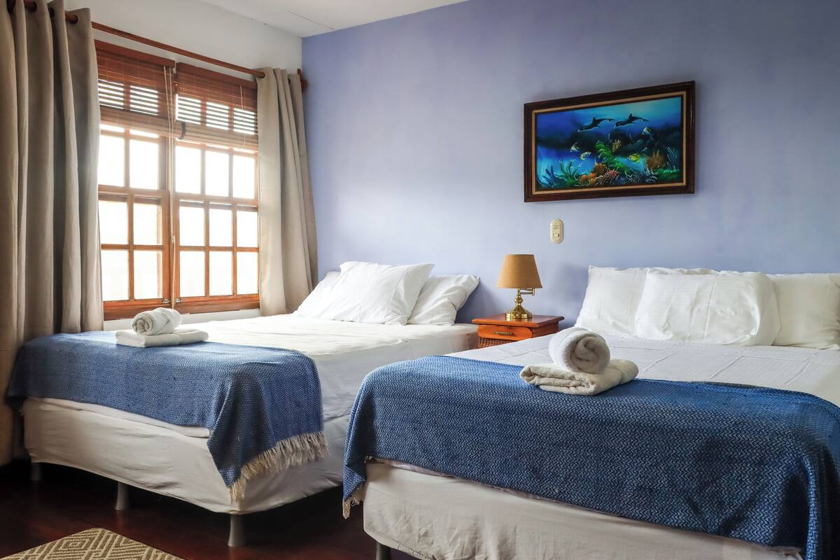 Une chambre d’hôtel avec deux lits, une fenêtre avec des rideaux, un tableau accroché au mur et une lampe de chevet.