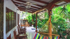 A covered patio with wooden chairs and a hammock, surrounded by lush greenery. - Hotel Gracia (San Juan del Sur)