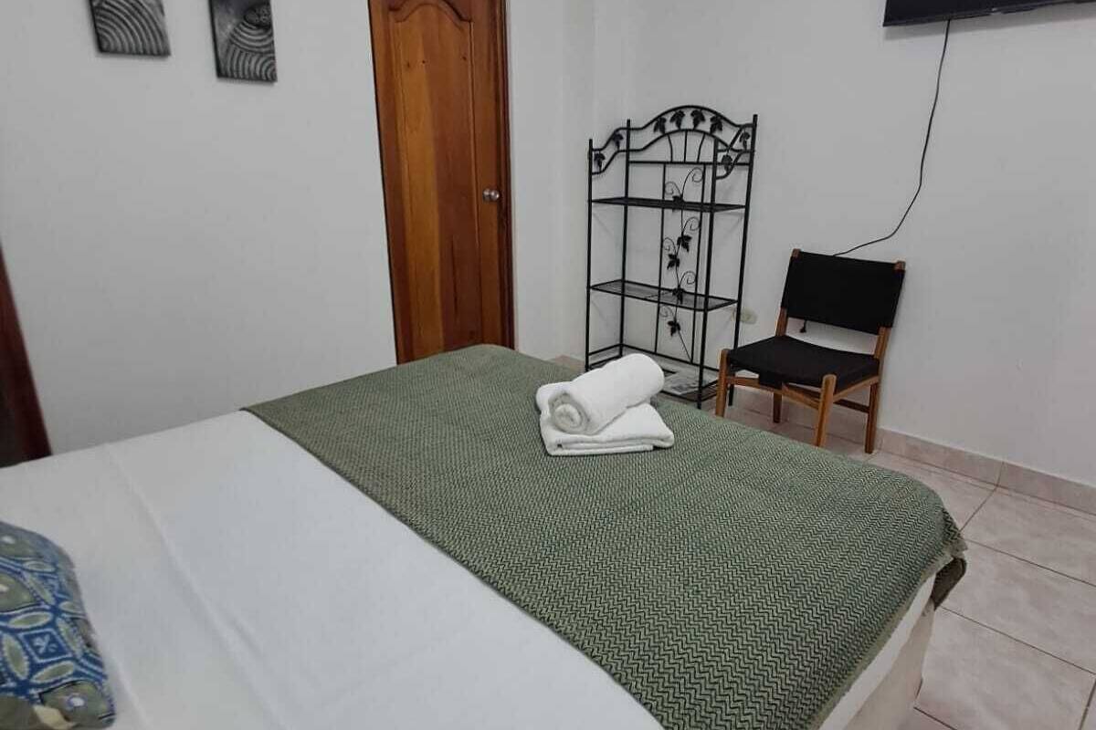 Une chambre à coucher avec un lit, une porte en bois, une étagère en métal, un téléviseur et une chaise.
