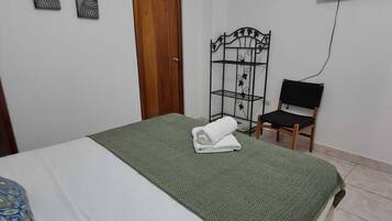 Une chambre à coucher avec un lit, une porte en bois, une étagère en métal, un téléviseur et une chaise.