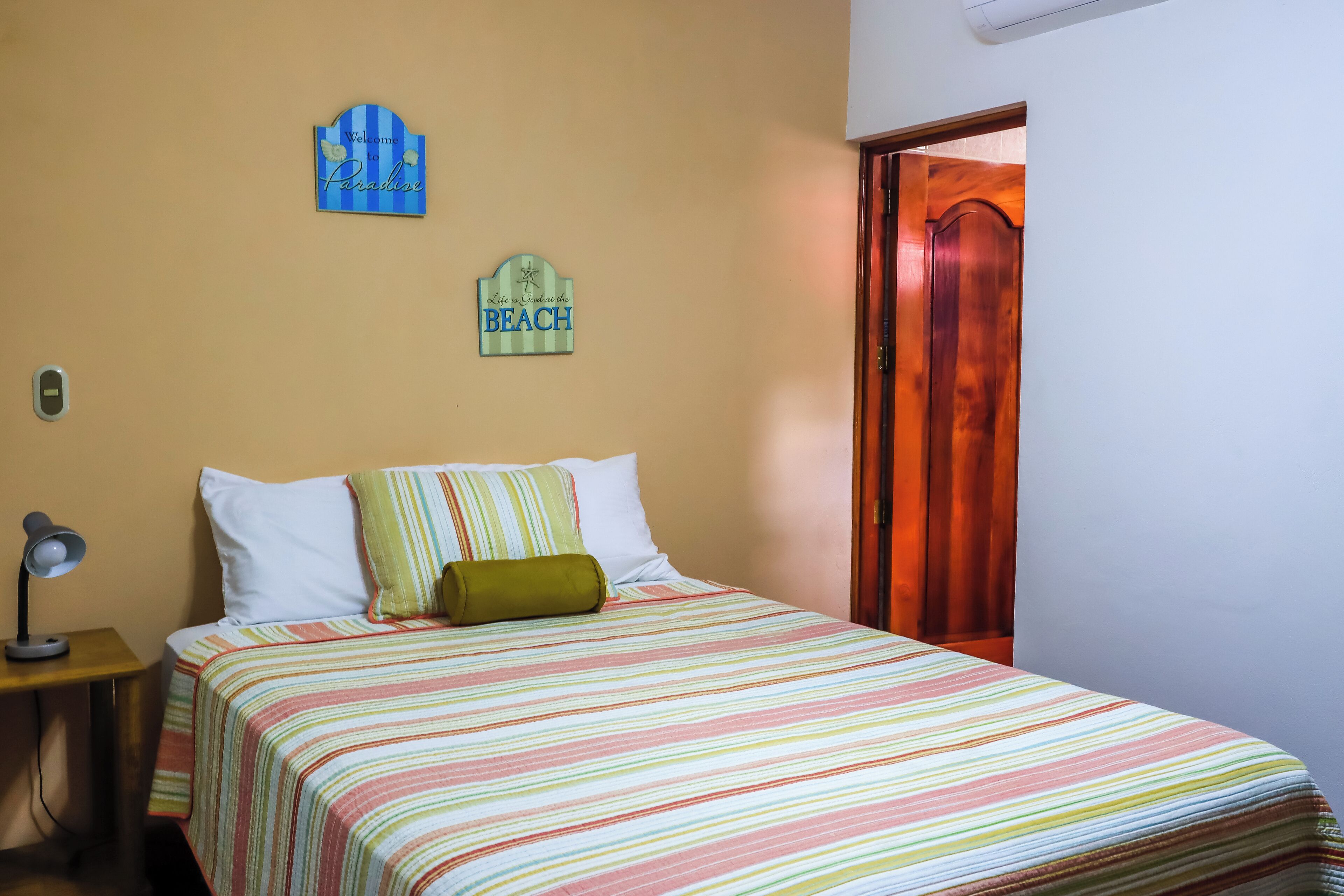 Un dormitori amb un llit, una tauleta de nit, una làmpada, una porta i dues decoracions murals.