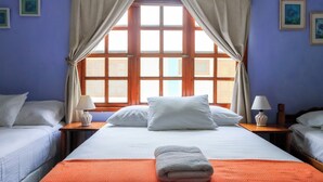 A hotel room with a large bed, two bedside tables with lamps, a window with curtains, and artwork on the walls. - Hotel Gracia (San Juan del Sur)